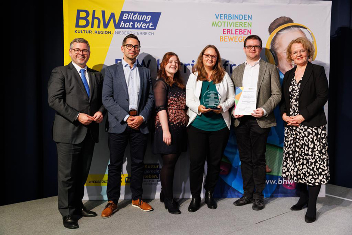 6 Personen stehen stolz vor einer Werbewand des BhW und pr&auml;sentieren einen Preis.