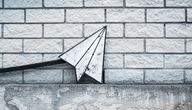 Wei&szlig;-graues Papieflieger-Icon vor einer wei&szlig;en Ziegelstein-Mauer