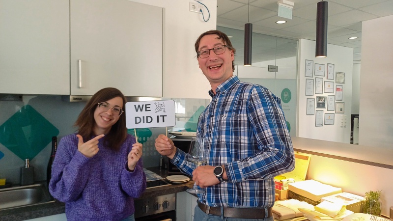 1 Frau und ein Mann stehen in einer Küche und halten ein Schild mit "We did it" in Händen
