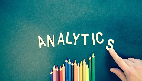 Der Schriftzug "Analytics" auf grünem Hintergrund mit einer Hand davor. Darunter Buntstifte.
