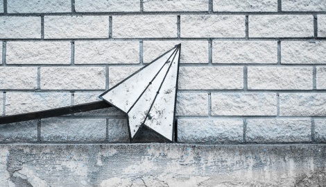Weiß-graues Papieflieger-Icon vor einer weißen Ziegelstein-Mauer