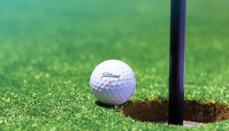 Golfball direkt vor einem Loch mit schwarzer Stange darin.
