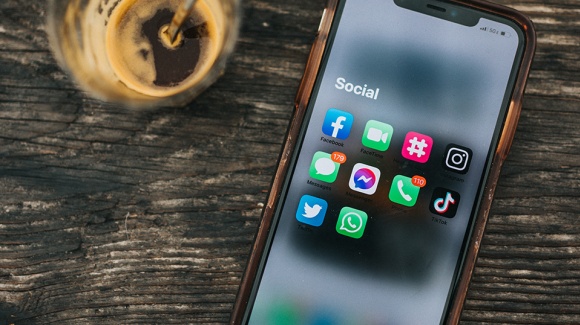 Ein iPhone liegt mit ge&ouml;ffnetem Social Men&uuml; auf einem Tisch, links davon ist ein Glas Kaffee