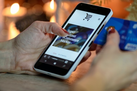Hand mit Handy auf dem ein Online-Shop abgebildet ist.