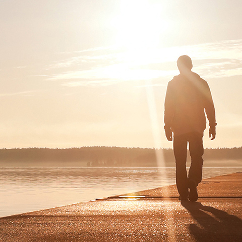 Ein Mann geht auf einem Steg den Sonnenuntergang entgegen.