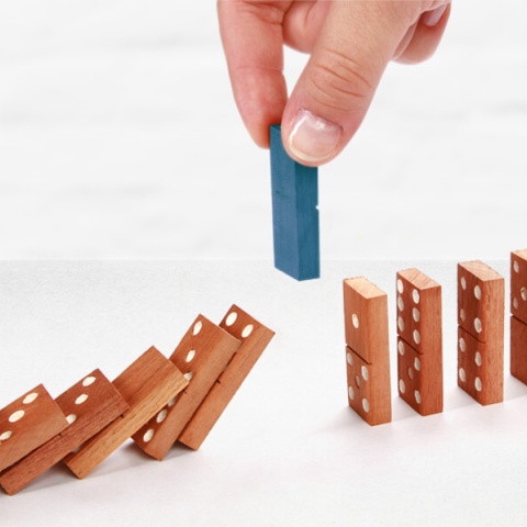 Eine Hand hält einen Dominostein über die Lücke einer Domino-Strecke