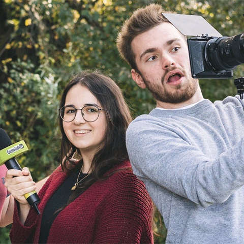 Eine Frau mit Mikrofon und ein Mann mit Filmkamera im Grünen.