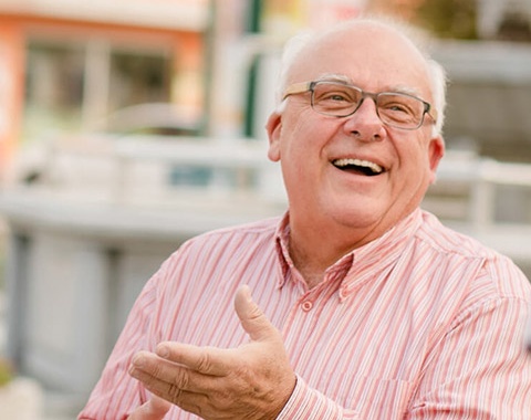 Ein &auml;lterer Herr mit Brille lacht herzlich. Er tr&auml;gt ein rot-wei&szlig; gestreiftes Hemd.