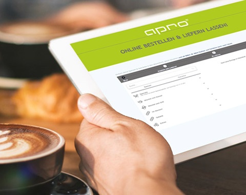 Eine Hand in einem Caf&eacute; h&auml;lt ein Tablet, darauf ist die Apro Website sichtbar.