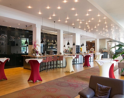 Man sieht die Bar des Cityhotel D&C mit sch&ouml;ner Beleuchtung, Stehtischen und Loungem&ouml;beln..