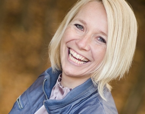 Eine Frau mit schulterlangen, blonden Haaren lacht herzlich in die Kamera.