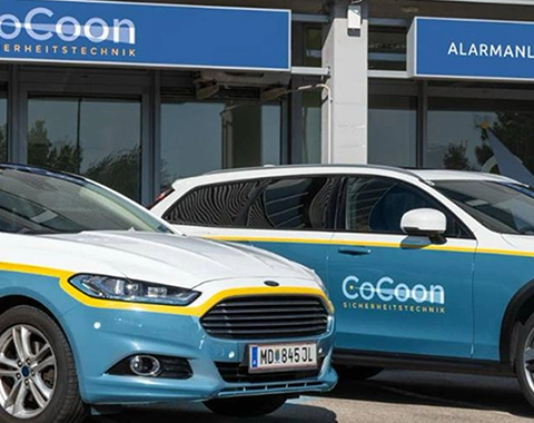 2 blau-gelbe Autos mit der Aufschrift "CoCoon" vor einem Autohaus