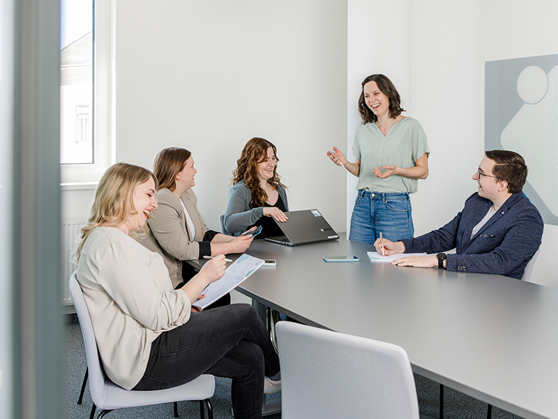 3 Frauen und 1 Mann sitzen um einen Konferenztisch, eine Frau tr&auml;gt etwas vor
