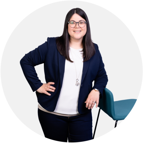 Theresa Memelauer steht an einem Arbeitsplatz und lächelt seitlich in die Kamera.