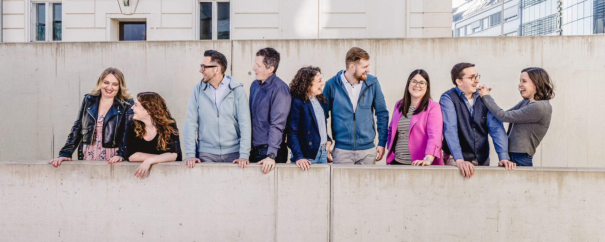 Das Q2E Team steht vor einer Betonmauer.