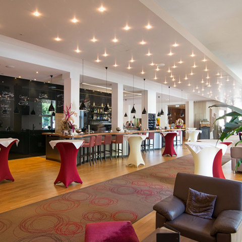 Man sieht die Bar des Cityhotel D&C mit schöner Beleuchtung, Stehtischen und Loungemöbeln..