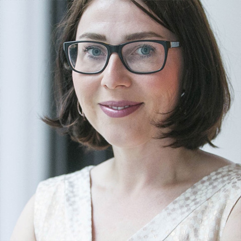 Eine dunkelhaarige Frau mit Brille lächelt in die Kamera.