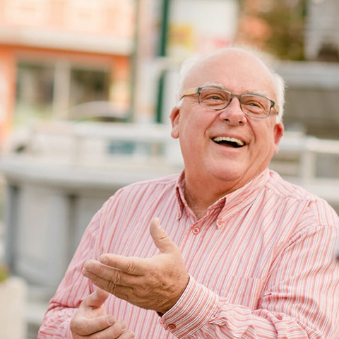 Ein älterer Herr mit Brille lacht herzlich. Er trägt ein rot-weiß gestreiftes Hemd.