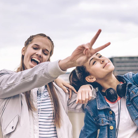 Zwei glückliche Mädchen die ein Selfie machen, eines macht mit der Hand das Victory-Zeichen.
