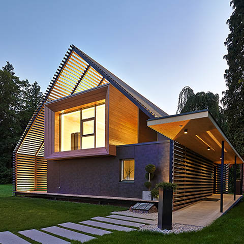 Abendaufnahme eines sehr modernen von innen beleuchteten Holzhauses.