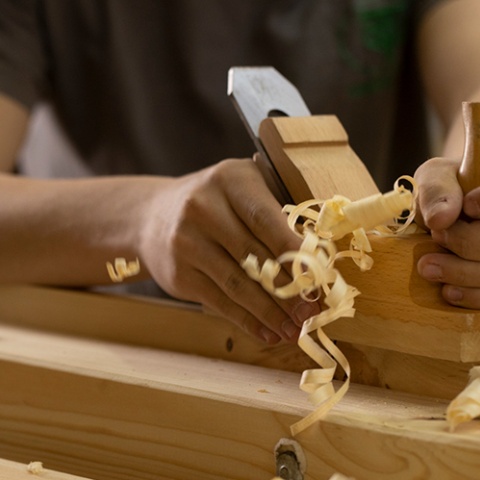 Hand hobelt ein Stück Holz, Späne fliegen weg